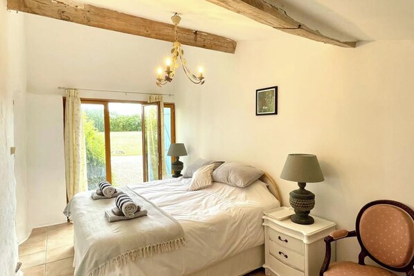 Ein Schlafzimmer mit einem großen Bett, zwei Nachttischen inklusive Lampen, einem Sessel und Blick auf einen Garten durch ein Fenster.