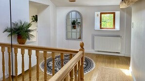 A staircase with wooden railings, a patterned rug, a potted plant, a window with a view, and a radiator. - Farmhouse Sleeps 11 with Shared Pool (Eymet)