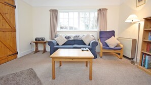 A living room with a sofa, a chair, a coffee table, a bookshelf, and a window with curtains.