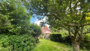 A well-maintained garden path leading to a house with a red roof, surrounded by lush greenery and trees.