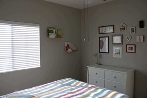 Een slaapkamer met een bed, een dressoir en een raam met jaloezieën.