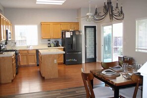 Una cocina moderna con armarios de madera, un refrigerador negro y un comedor con una mesa dispuesta para cuatro comensales.