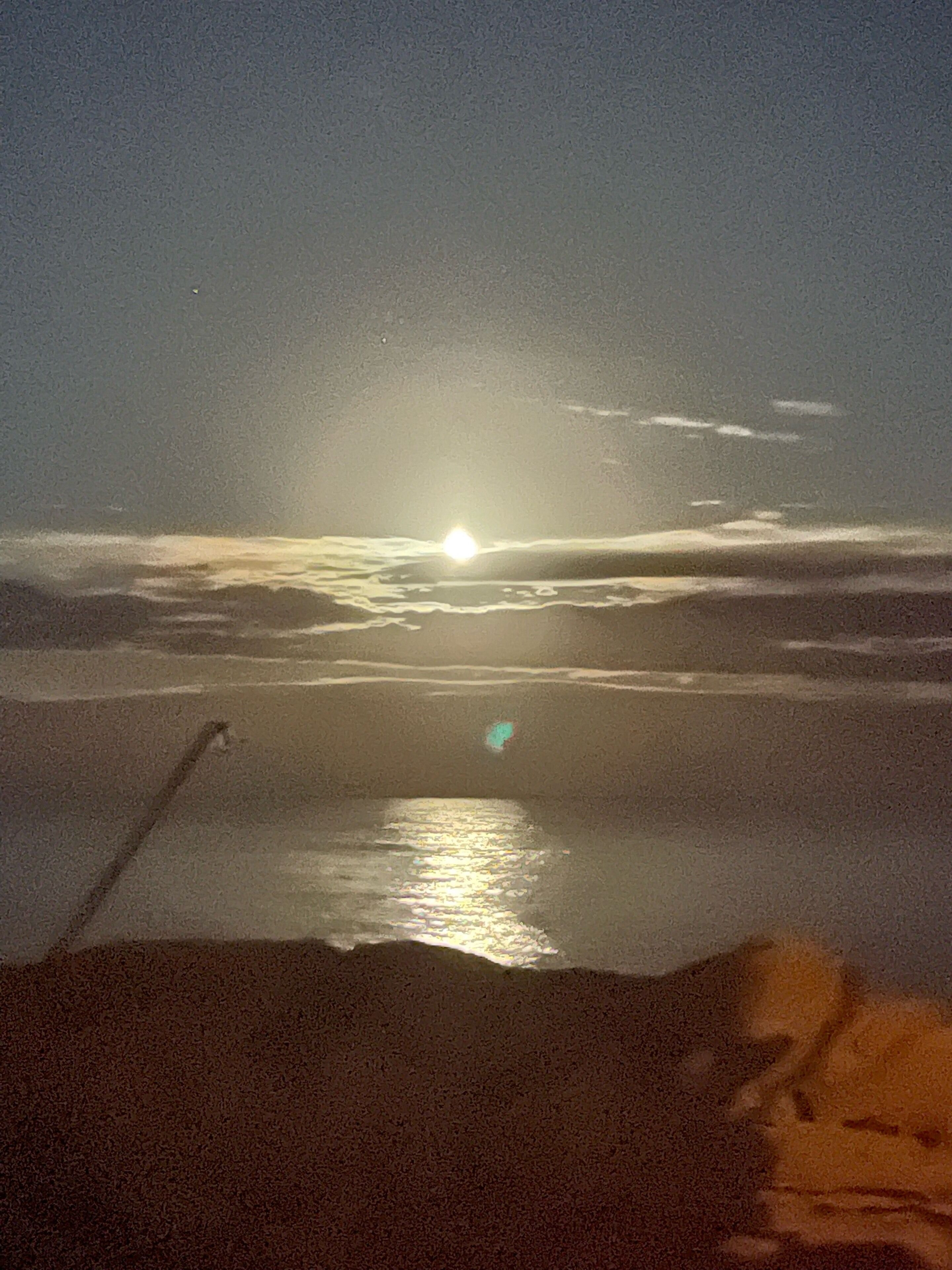 Une scène de plage où le soleil se couche sur l’eau, créant un reflet à la surface.