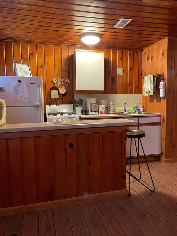 A wooden-paneled kitchen with a refrigerator, stove, coffee maker, and various kitchen items on the counter.