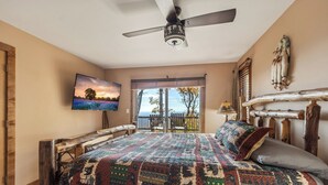 A bedroom with a large bed, a ceiling fan, a TV mounted on the wall, and a balcony with a view of trees and a sunset. - Enjoy mountain views, cook out on the Weber grill & relax! - Canoe Believe It (Jasper)