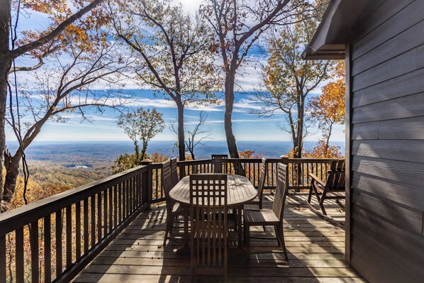 Une terrasse en bois avec une table et des chaises, offrant une vue sur un paysage montagneux.
