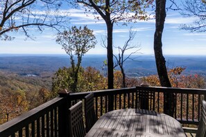 Une terrasse en bois avec une table et des chaises, offrant une vue sur un paysage montagneux.