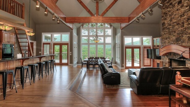 A spacious living area with a high ceiling, wooden beams, a fireplace, and large windows offering a view of the outdoors. - Fireside Sips, Soothing Hot Tub Soaks, Hiking Trails, Lakeside Dining & Scenic Golf - Field of Stars (Jasper)