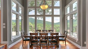 A dining room with a large table and chairs, large windows with a view of green hills, and a hanging light fixture. - Fireside Sips, Soothing Hot Tub Soaks, Hiking Trails, Lakeside Dining & Scenic Golf - Field of Stars (Jasper)