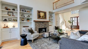 A spacious living room with a stone fireplace, a high ceiling, and a staircase leading to an upper level. - Hillside Manor - Luxury Hot Tub + Fireplace + Pool Table + & Wet Bar (Jasper)