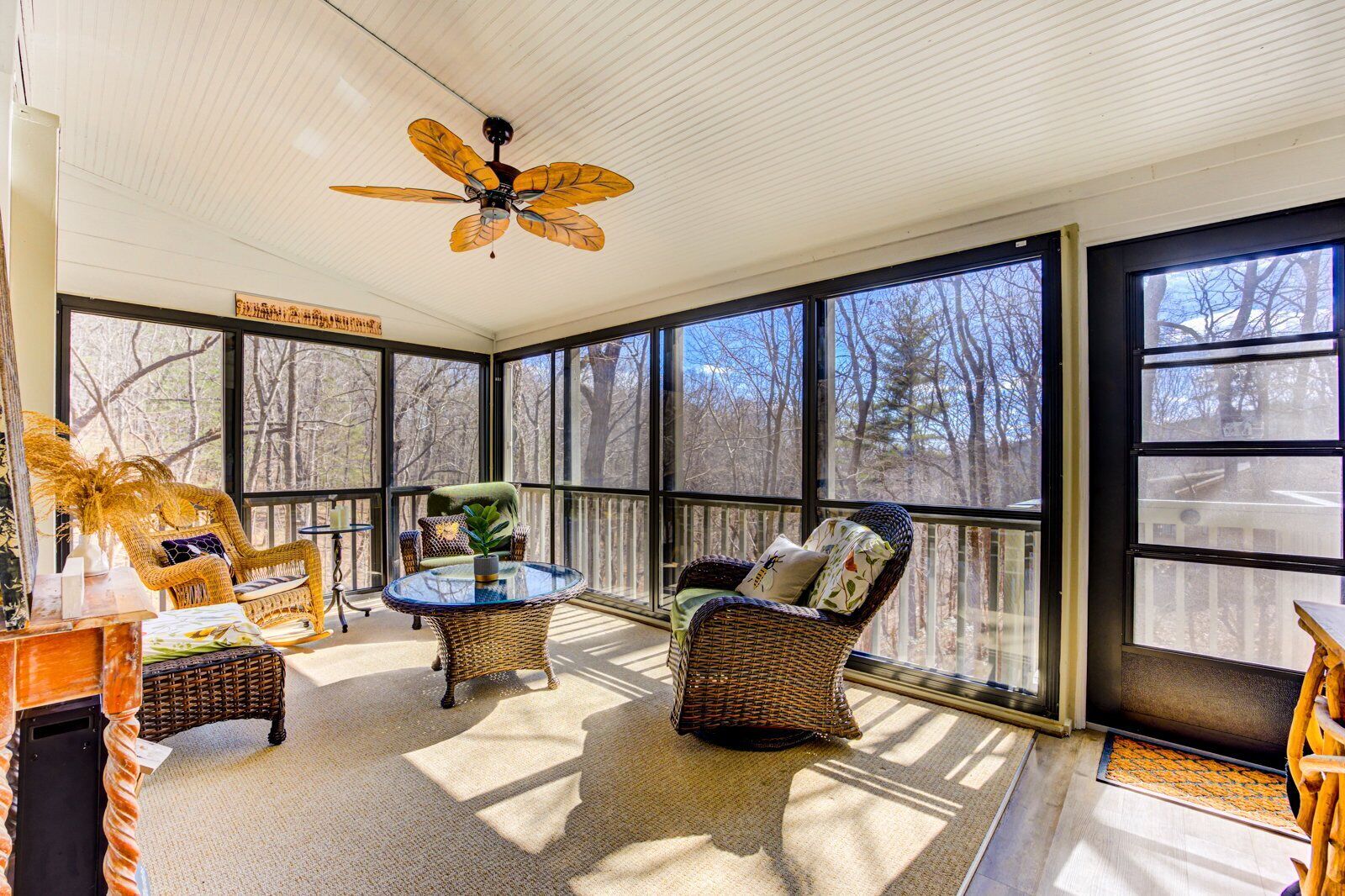 A sunroom with wicker furniture, large windows, and a ceiling fan.