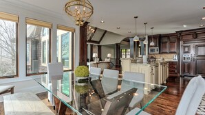 A spacious kitchen with dark wood cabinets, a central island, and a dining area with a glass table and chairs. - MountainView - Mountain luxury in Big Canoe! (Jasper)