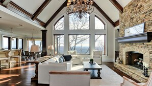 A spacious living room with a stone fireplace, large windows, and a high ceiling with exposed beams. - MountainView - Mountain luxury in Big Canoe! (Jasper)