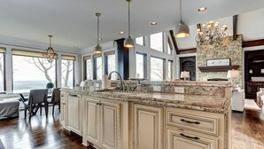 A spacious kitchen with a large island, granite countertops, and a stone backsplash. There are multiple pendant lights and a chandelier. - MountainView - Mountain luxury in Big Canoe! (Jasper)