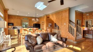 A spacious living room with a leather sofa, wooden dining table, and a kitchen in the background. - Paradise Retreat - Sip Cocktails by Lake Disharoon, Play Golf & Swim Year-Round (Jasper)