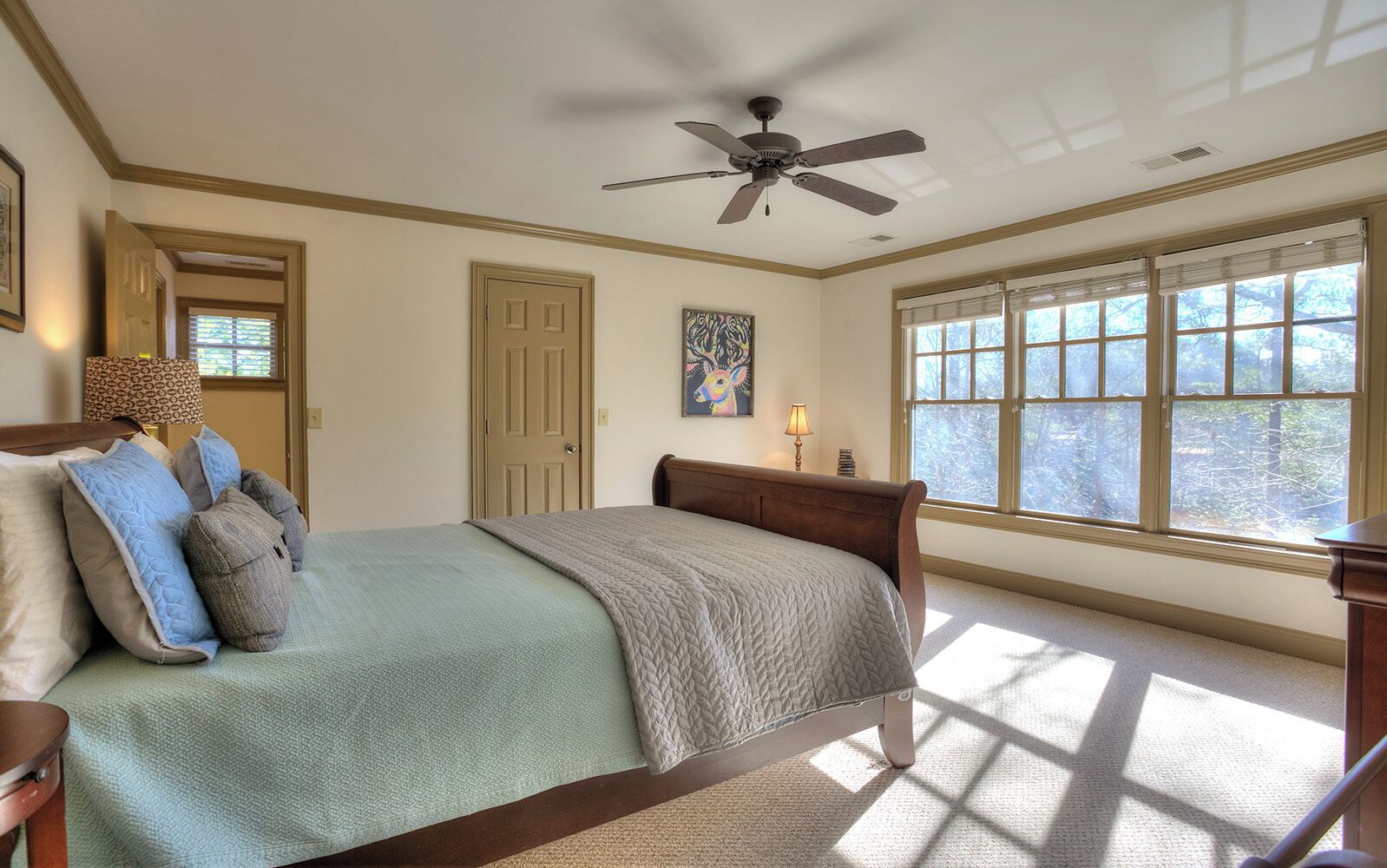 A bedroom with a bed, a ceiling fan, a window with blinds, and a door.
