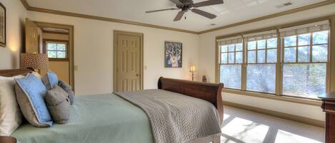 A bedroom with a bed, a ceiling fan, a window with blinds, and a door.