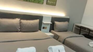 Habitación de hotel con dos camas, cada una con colcha y almohadas grises. Hay dos toallas sobre las camas y la habitación presenta un diseño moderno con un cuadro abstracto grande en la pared.