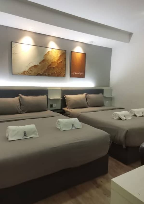 Habitación de hotel con dos camas, cada una con una almohada y una toalla. Hay luces empotradas en la pared y un cuadro abstracto grande sobre las camas.
