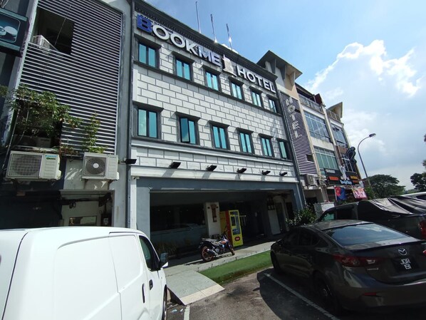 Hotel com fachada moderna, várias janelas e estacionamento com carros e uma van.