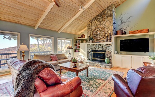 A cozy living room with a stone fireplace, leather furniture, and a large flat-screen TV.