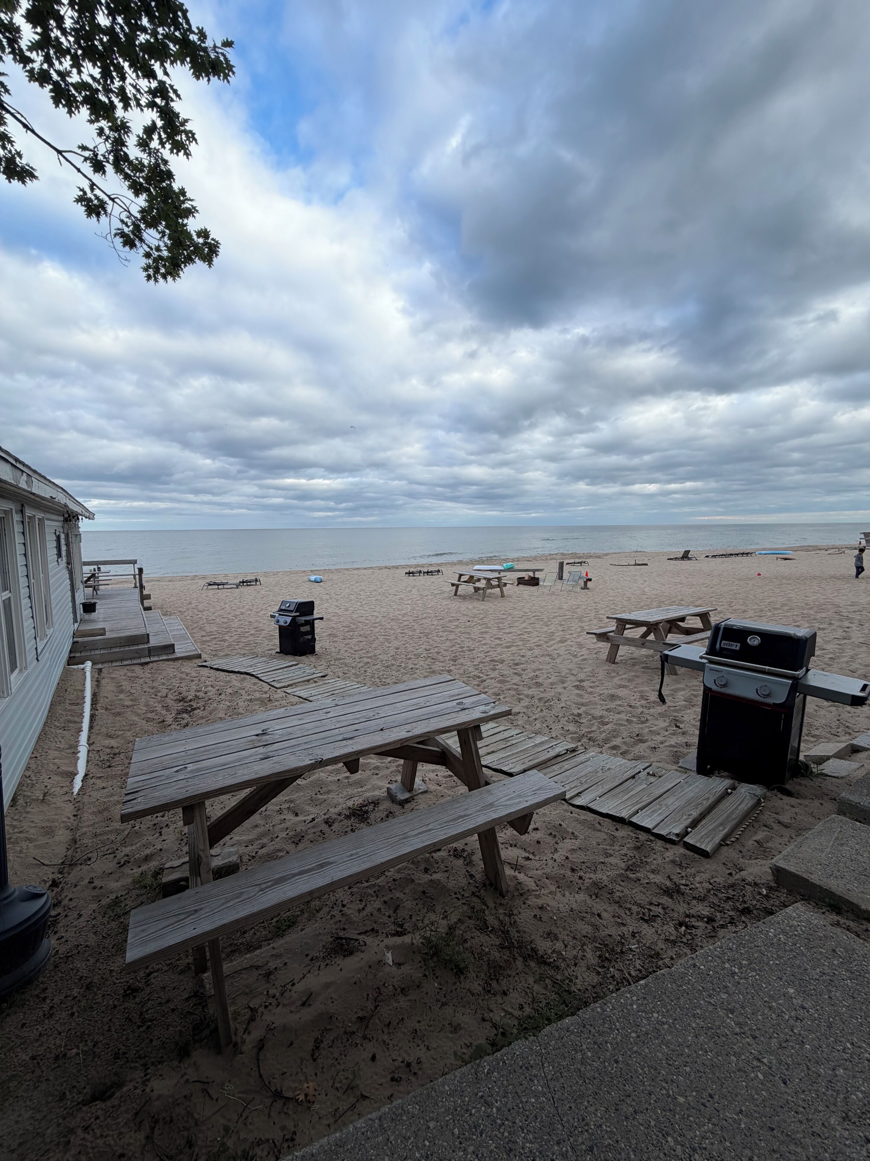 A beach with picnic tables and a barbecue grill.