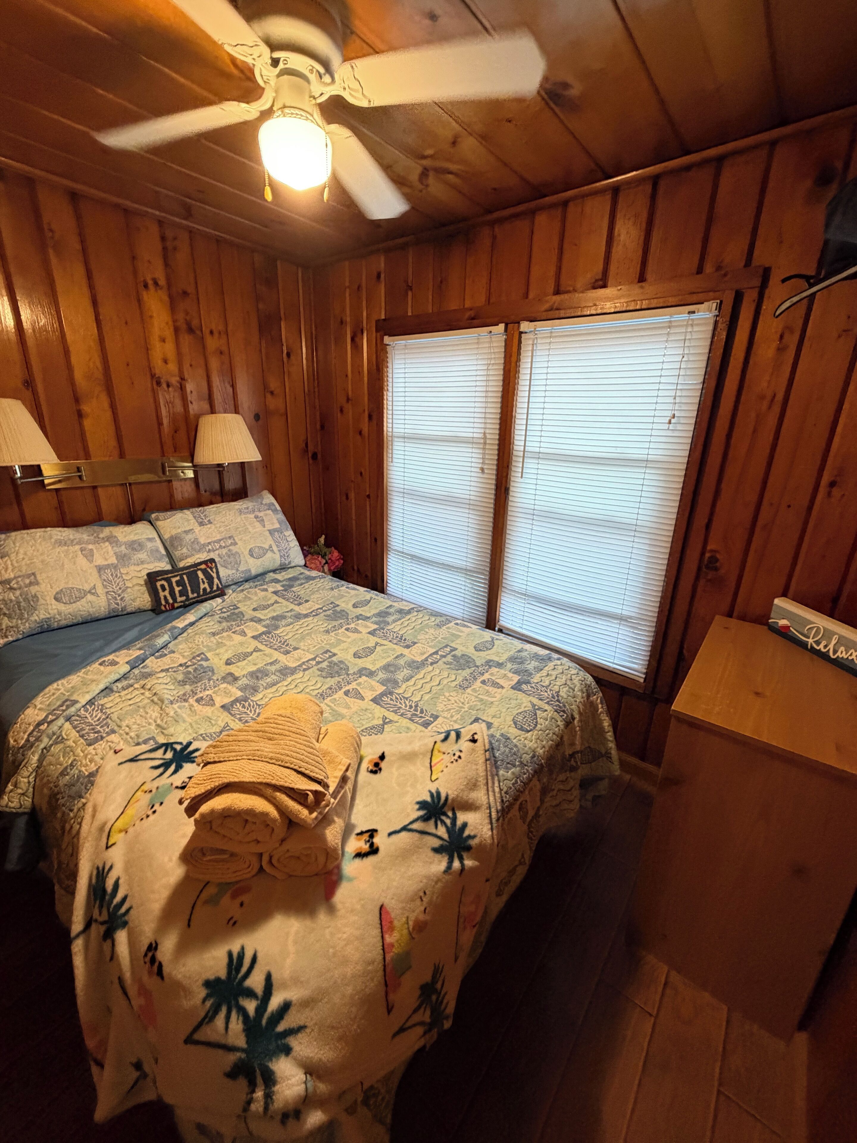 A room with a bed, two lamps, a ceiling fan, and a window with blinds.