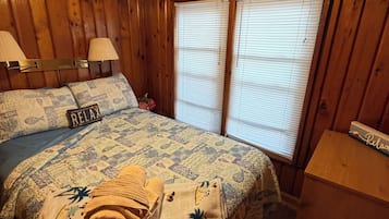 A room with a bed, two lamps, a ceiling fan, and a window with blinds.
