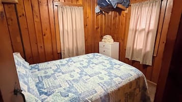A bedroom with a bed, a ceiling fan, a nightstand, and a window with curtains.
