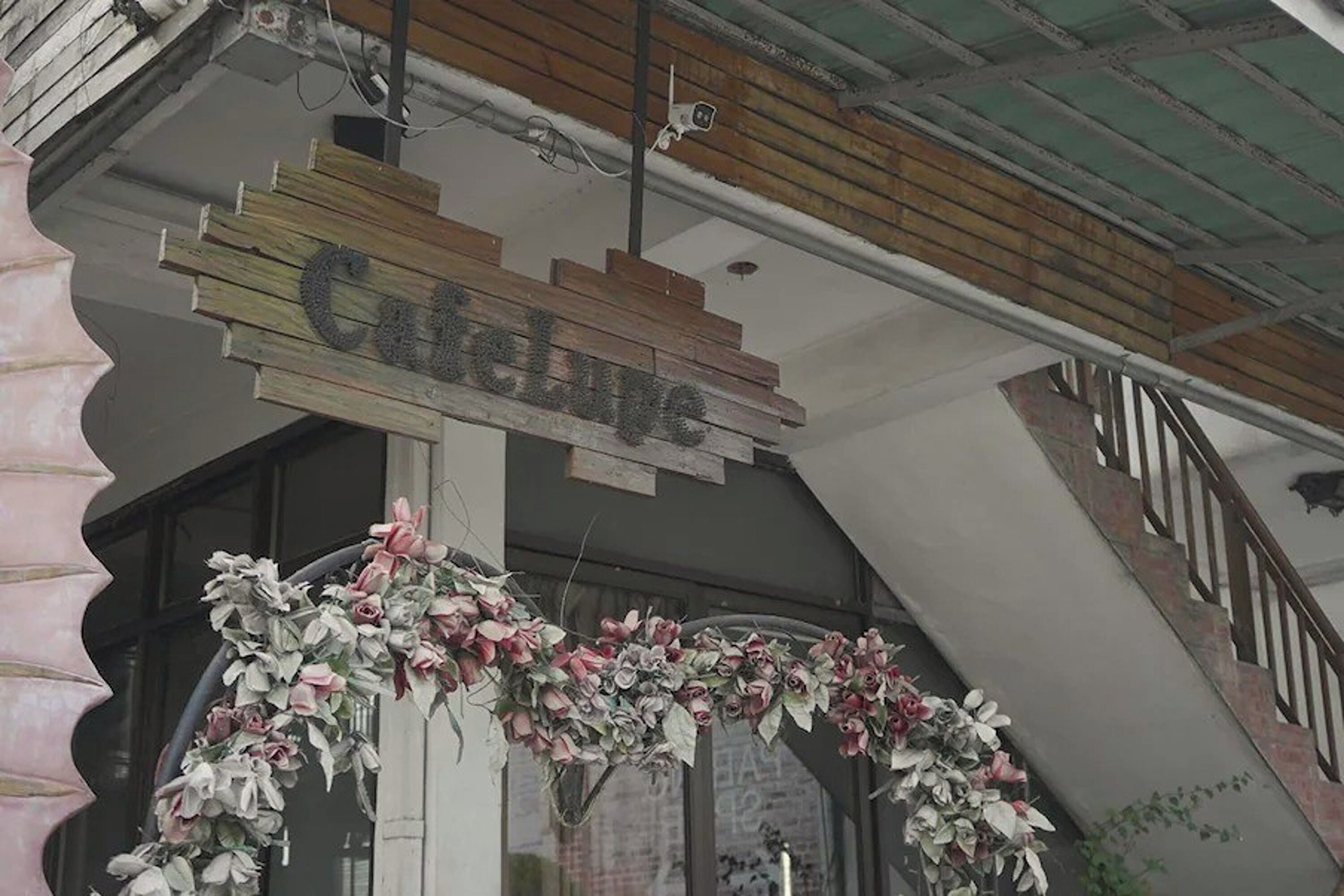 A storefront with a wooden sign reading "Cafe du Jour" and floral decorations around the entrance.