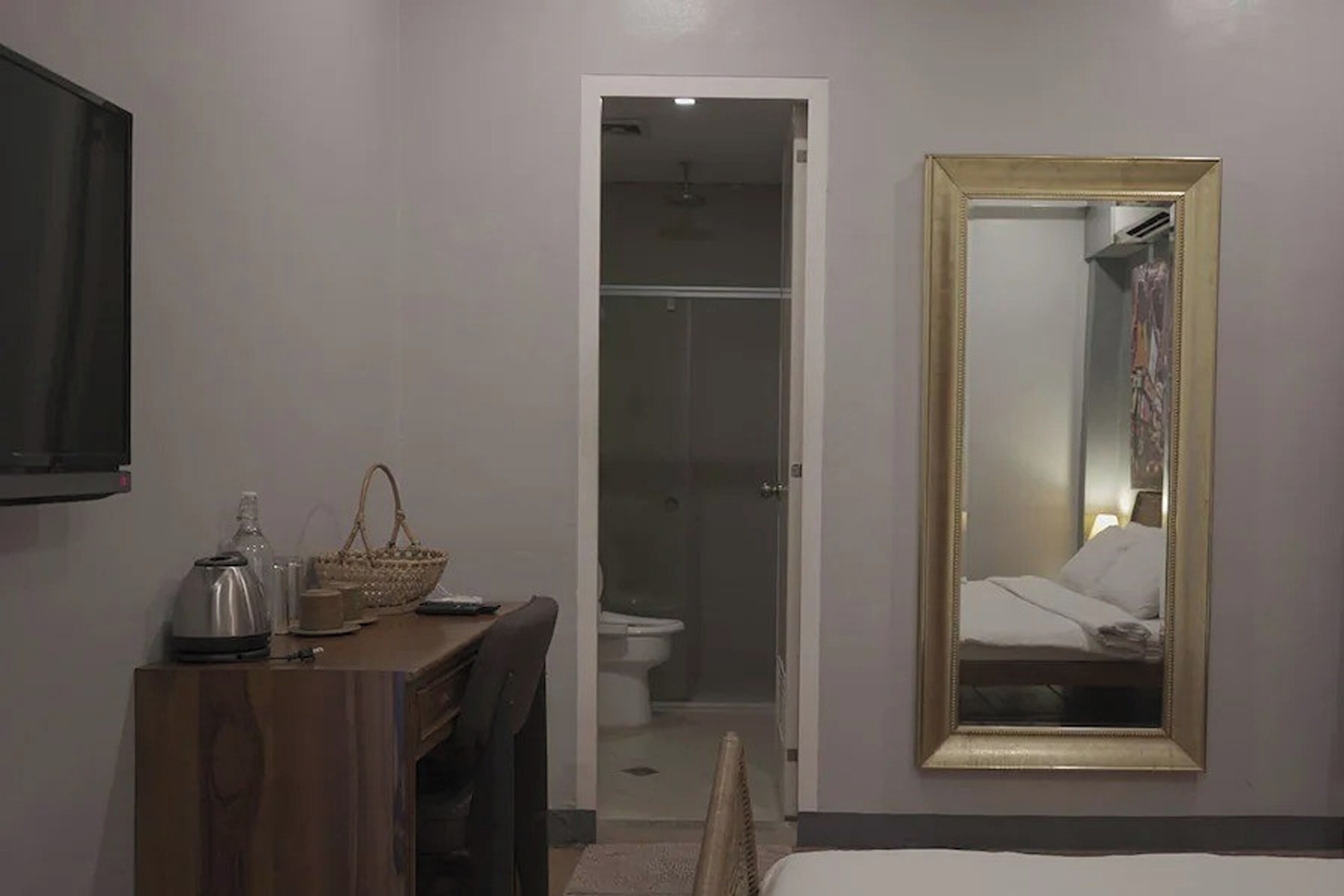 A hotel room with a wooden desk, a mirror, a shower, and a bed.