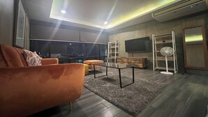 A modern living room with a sofa, ottoman, coffee table, TV, and a fan. - Casa Alegria Bed and Breakfast Antipolo (Antipolo)