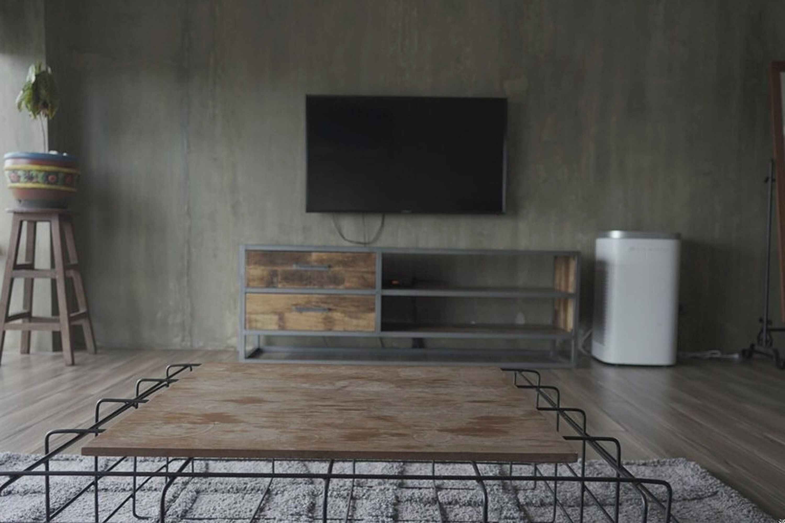 A modern living room with a wooden coffee table, a TV mounted on the wall, and a white cabinet.