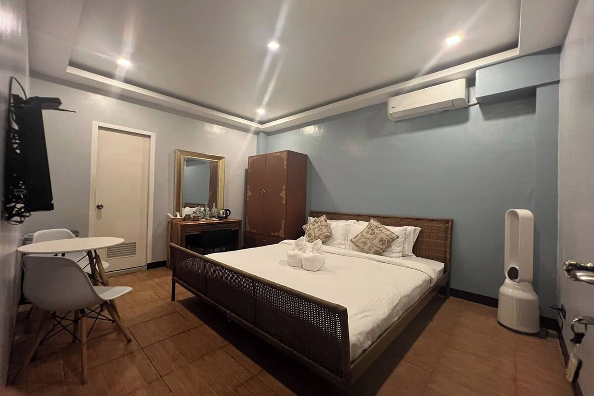 A hotel room with a bed, a small table, chairs, a wardrobe, and a mirror.