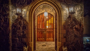 A stone archway with wooden doors and two wall-mounted lanterns.