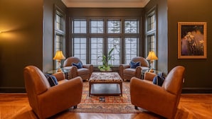 A room with two leather armchairs, a patterned ottoman, and a large window with multiple panes.