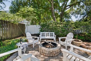 A patio with Adirondack chairs, a fire pit, and a white bench.