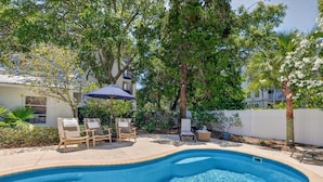 Una piscina con lettini, un ombrellone e alberi circostanti.