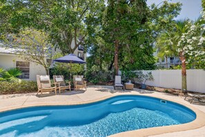 A swimming pool with lounge chairs, a patio umbrella, and surrounding trees.