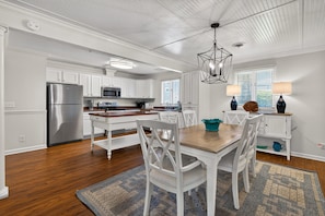 A kitchen with white cabinets, stainless steel appliances, and a wooden dining table with white chairs.