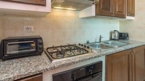 A kitchen with wooden cabinets, a gas stove, a built-in oven, a toaster, and a sink. - Li Cossi by Interhome (Costa Paradiso)