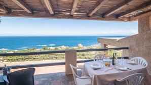 An outdoor dining area with a view of the ocean, featuring a table set for two with white chairs, a pergola overhead, and a stone wall. - Li Cossi by Interhome (Costa Paradiso)