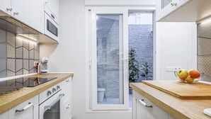 Una cucina moderna con mobili bianchi, un piano di lavoro in legno e vista su una zona esterna attraverso una porta in vetro.