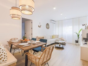 Un salon moderne avec un coin repas, comprenant des meubles en osier, un canapé, une table basse et des luminaires suspendus.