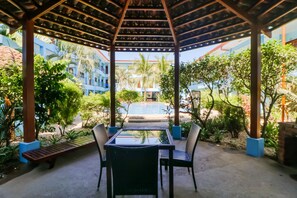 A covered outdoor seating area with a pool in the background.