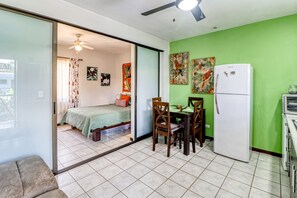 A room with a bed, a dining table with chairs, a refrigerator, and a ceiling fan.