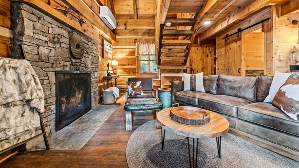 A cozy log cabin interior with a stone fireplace, wooden walls, a leather sofa, and a round wooden coffee table. - Retreat that will have you wanting more RELAxATION (Sevierville)