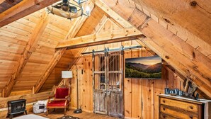 A cozy attic bedroom with a sloped ceiling, a red chair, a wooden dresser, and a scenic landscape painting. - Retreat that will have you wanting more RELAxATION (Sevierville)