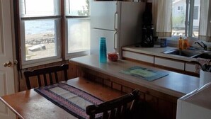 Eine kleine Küche mit Holzwänden, einem weißen Kühlschrank, einer Spüle und einem Fenster mit Blick auf den Strand.