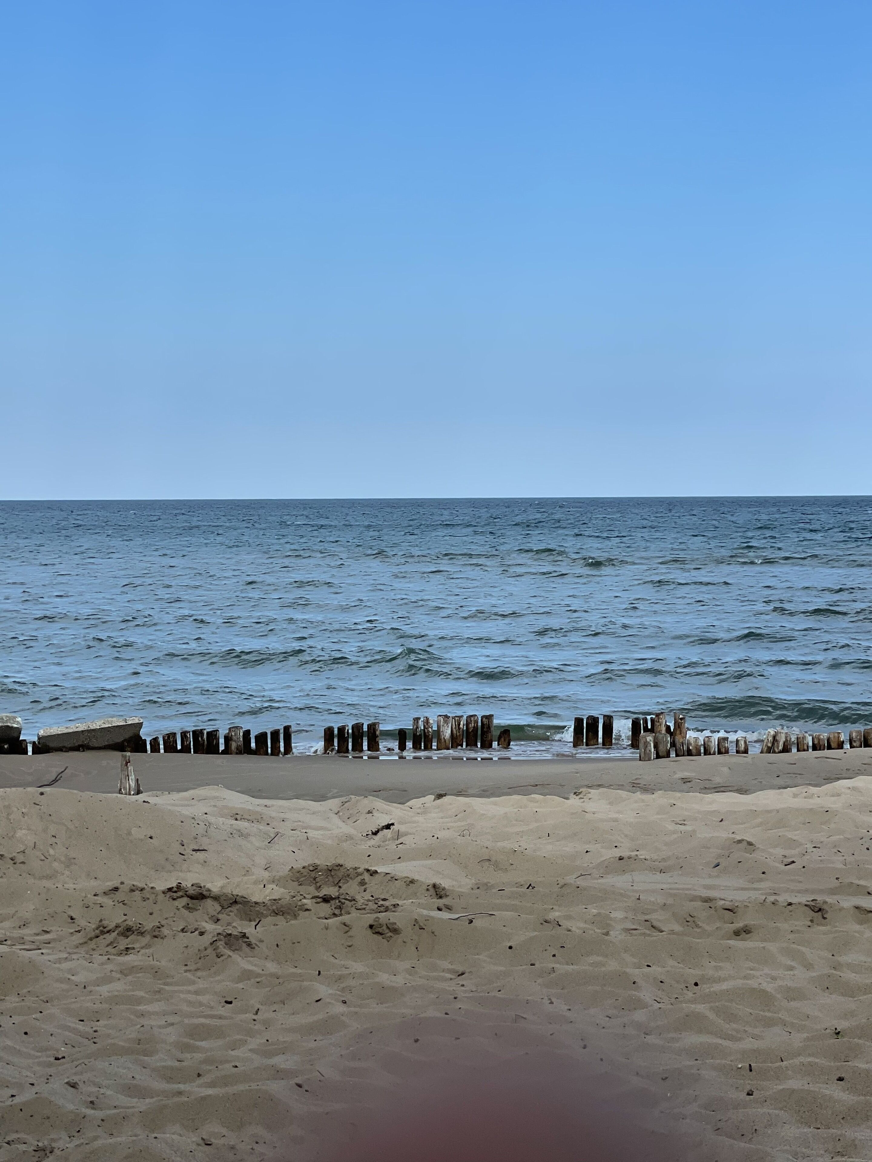 A beach with a wooden breakwater and calm sea.